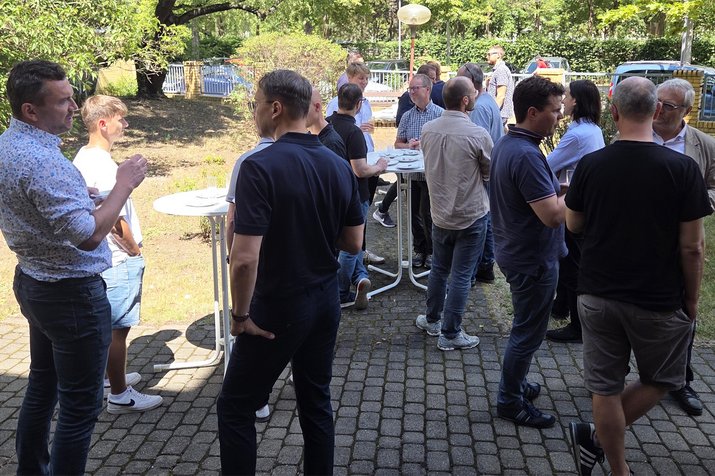 Personen stehen zusammen bei Getränken und Snacks im Garten bei Sonne