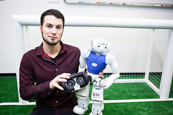Nao-Team-HTWK-Mitglied Marcel Göbe mit Fußballroboter Informatik-Absolvent Marcel Göbe hält einen Nao-Roboter sowie eine VR-Brille in den Händen.