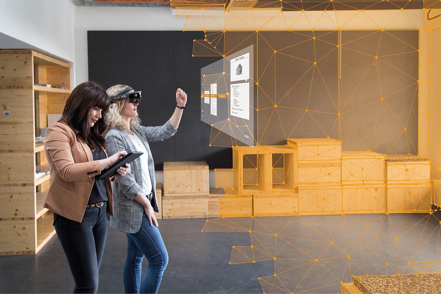 Aufmaß mit der HoloLens Sophie Seifert klickt auf ein Tablet, Lena Salm trägt eine HoloLens und klickt in die Luft auf einen Bildschirm, der in der Luft schwebt. Im Hintergrund sieht man einen Raum, dessen Kanten digital nachgezeichnet wurden.