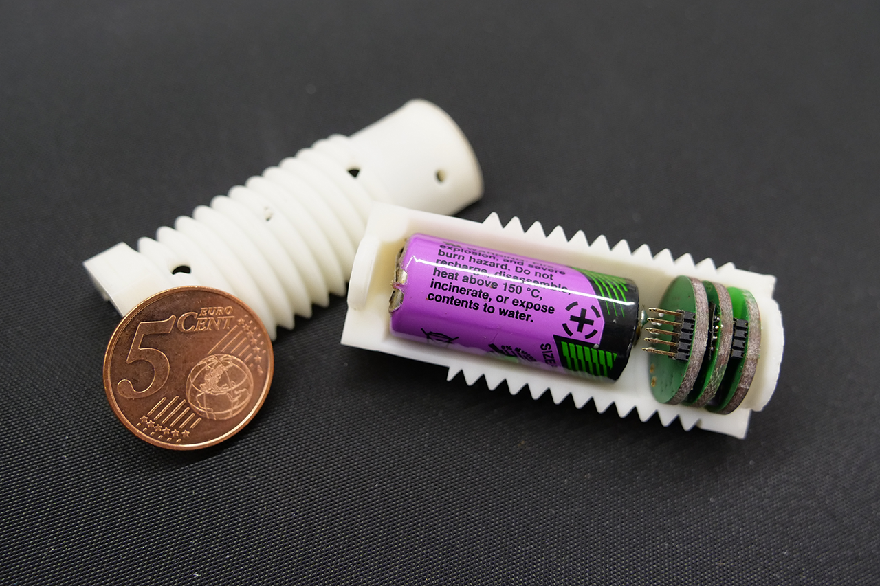 Sensor mit Batterie in heller aufgeschnittener Schraubenform, daneben 1 Cent-Münze